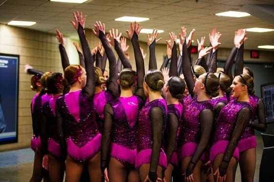 2014-2015 Lightning Dance Team in purple and black uniforms, posing backstage with raised hands.