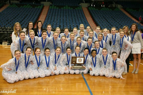 2013-2014 Lightning Dance Team posing with their championship trophy in white costumes.
